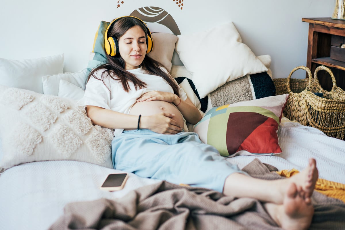 Pregnant Woman on Bed Listening to Music with Headphones