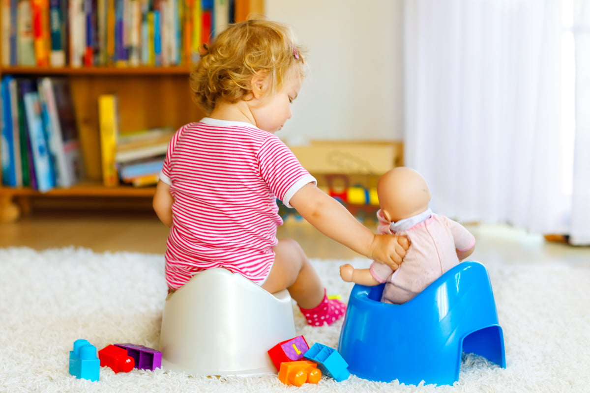 Close-up of cute little 12 months old toddler baby girl child sitting on potty. Kid playing with doll toy. Toilet training concept. Baby learning, development steps